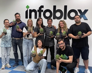 A team of nine employees smiling and holding terrariums while posing in front of a wall with the Infoblox logo.
